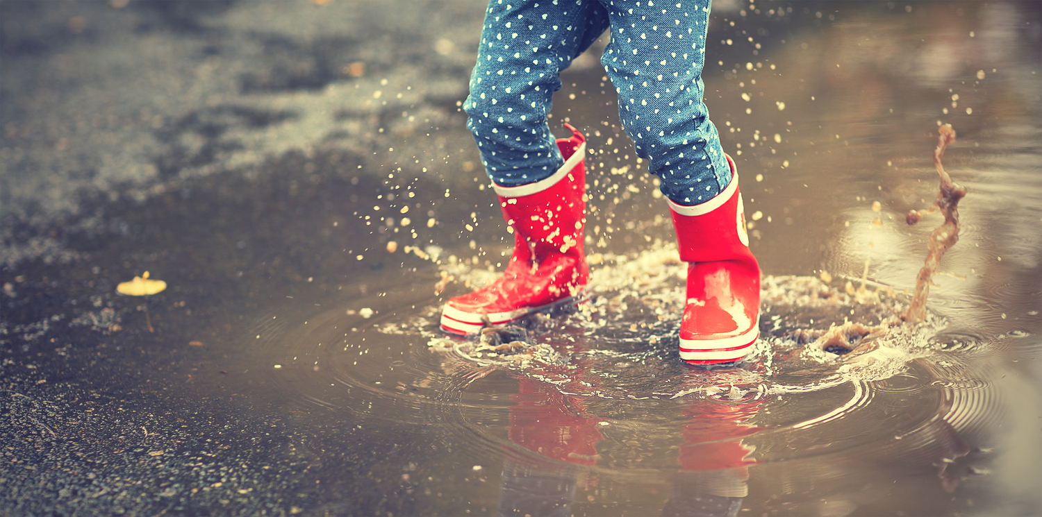 Person in rain boots splashing in a puddle.