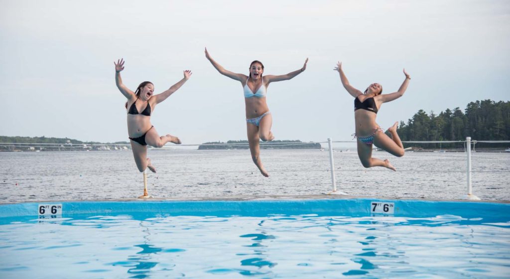 Three young women jumping into the pool.