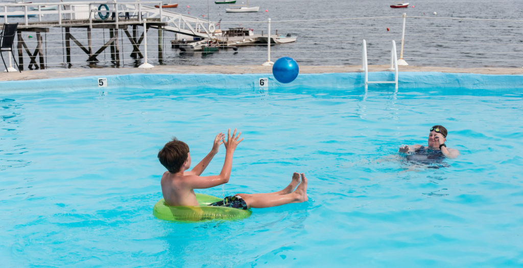 Two young people playing catch in the pool.