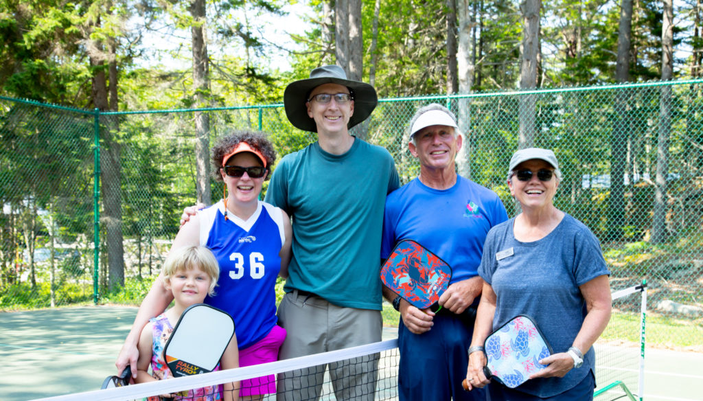 Family on a tennis court holding pickleball paddles.