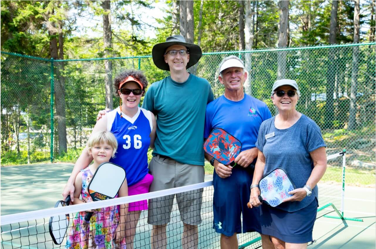 Family on a tennis court holding pickleball paddles.
